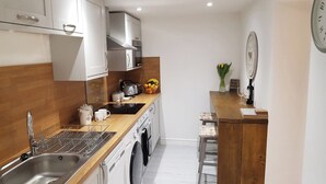 A compact kitchen with a sink, stove, microwave, and a wooden countertop. - Cottage Apartment - UK2774 (Llandudno)