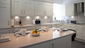 A modern kitchen with white cabinets, a central island with fruits and cups, a microwave, and a toaster. - This stunning Victorian property has just finished a full renovation. (Elgin)