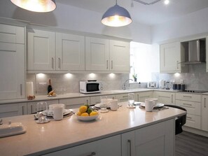 Een moderne keuken met witte kasten, een centraal eiland met fruit en bekers, een magnetron en een broodrooster.