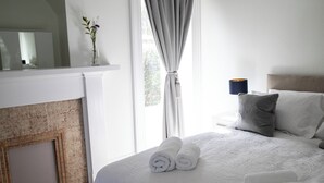 A neatly made bed with rolled towels, a bedside lamp, and a view of a window with curtains. - This stunning Victorian property has just finished a full renovation. (Elgin)