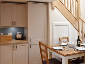 A dining area with a wooden table set for two, a chair, a bread box, a radio, and a wine bottle. - 2 bedroom accommodation in By Dunkeld, Pitlochry (By Dunkeld, Pitlochry)