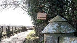 Placa com a inscrição 'Mill Cottage No Through Road', com uma estrutura de pedra ao lado.