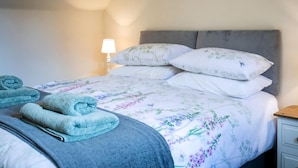 Cama bem arrumada com roupa de cama floral, luminária de cabeceira e toalhas dobradas sobre a cama.