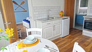 Cocina pequeña con gabinetes blancos, un lavabo y una estufa. Hay una mesa de comedor dispuesta con platos, vasos y cubiertos.
