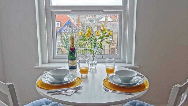 Une table dressée pour un dîner à deux, avec une bouteille de champagne, des verres et un vase rempli de fleurs jaunes.