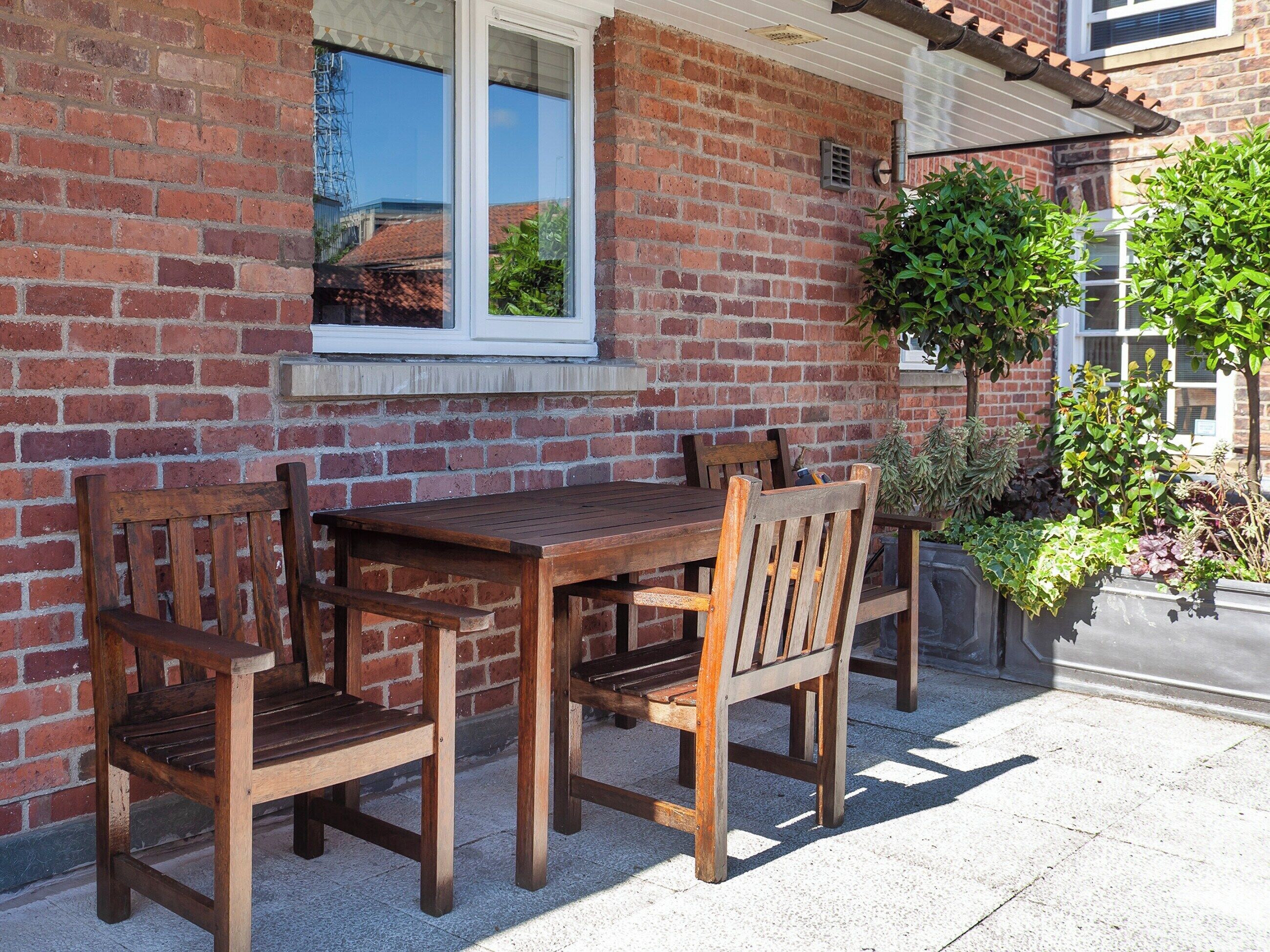A wooden table and chairs set against a brick wall with a window above.