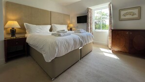 A neatly made bed with white linens and towels, a bedside table with a lamp, a television mounted on the wall, and a window with curtains. - Balloan House-UK7383 (Dornoch)