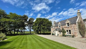 A stone building with a well-maintained lawn and trees in the background. - Balloan House-UK7383 (Dornoch)