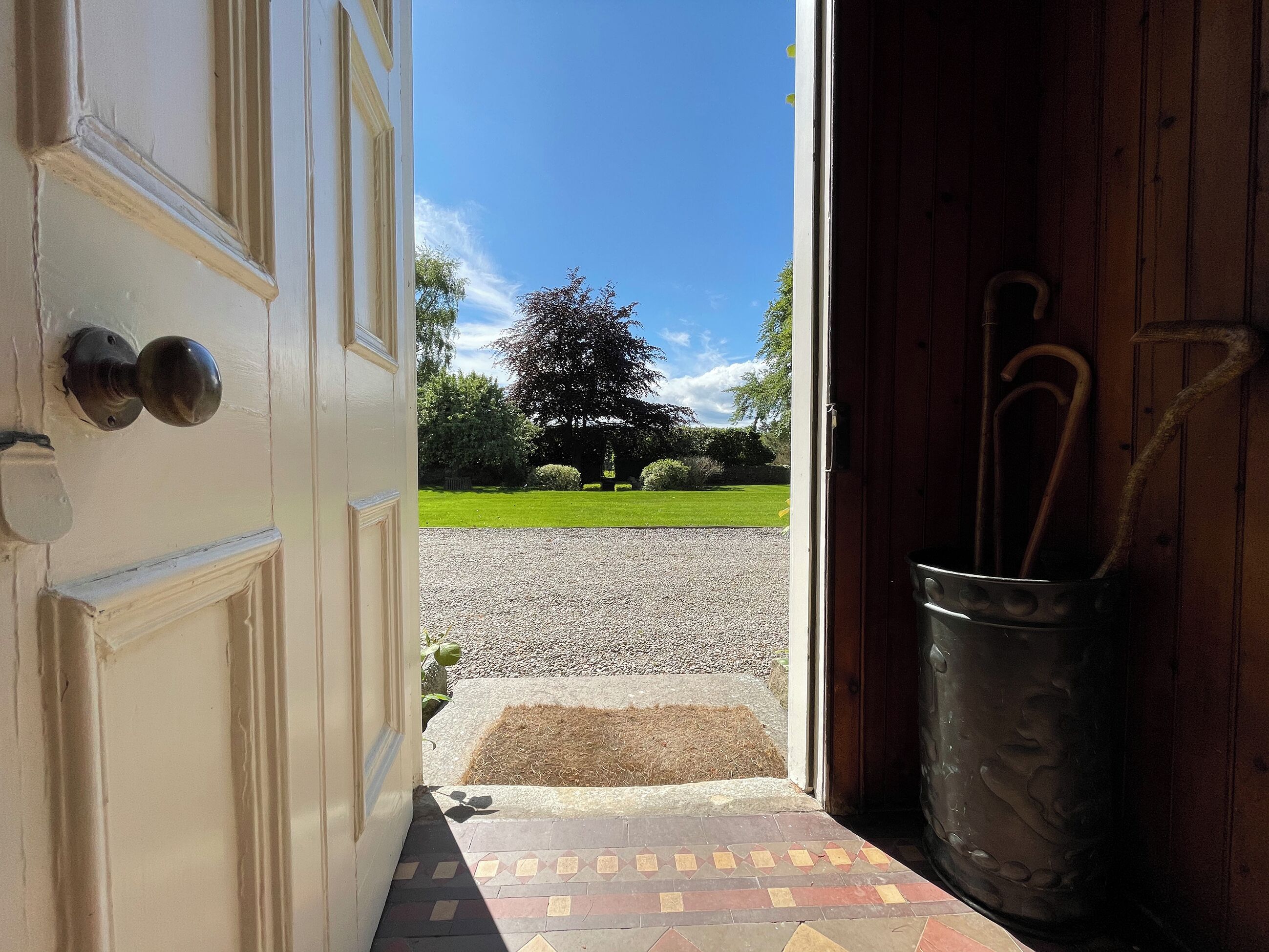 An open door leading to a gravel path with a green lawn and trees in the background.