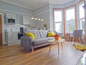 A modern kitchen with white cabinets, a grey sofa, and a dining area with a table and chairs. - 2 bedroom accommodation in Llandudno (Llandudno)