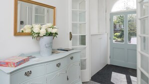 En hall med en vit byrå, en spegel och en vas med vita blommor.