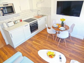 Una cocina moderna con armarios blancos, horno empotrado y comedor con una mesa para dos.