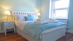 A neatly made bed with a blue blanket, white pillows, and two bedside tables with lamps.