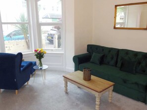 A living room with a green sofa, a blue armchair, a small round table, and a vase of flowers. - Snowdon Retreat Villa (Llandudno)