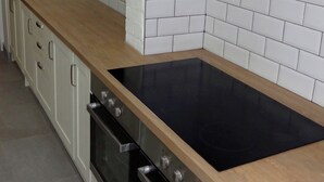 Een keuken met een zwart fornuis, witte kastjes en een houten aanrecht.