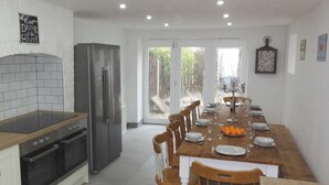 Een moderne keuken met een eethoek, met een roestvrijstalen koelkast, een houten eettafel gedekt voor vier personen, en een groot raam met uitzicht op de omgeving.