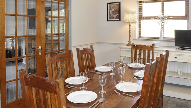 A dining table set for six with wooden chairs, a chandelier, and a television in the background. - Ty Fynnon Cottage-UK2786 (Penmaenmawr, near Conwy)