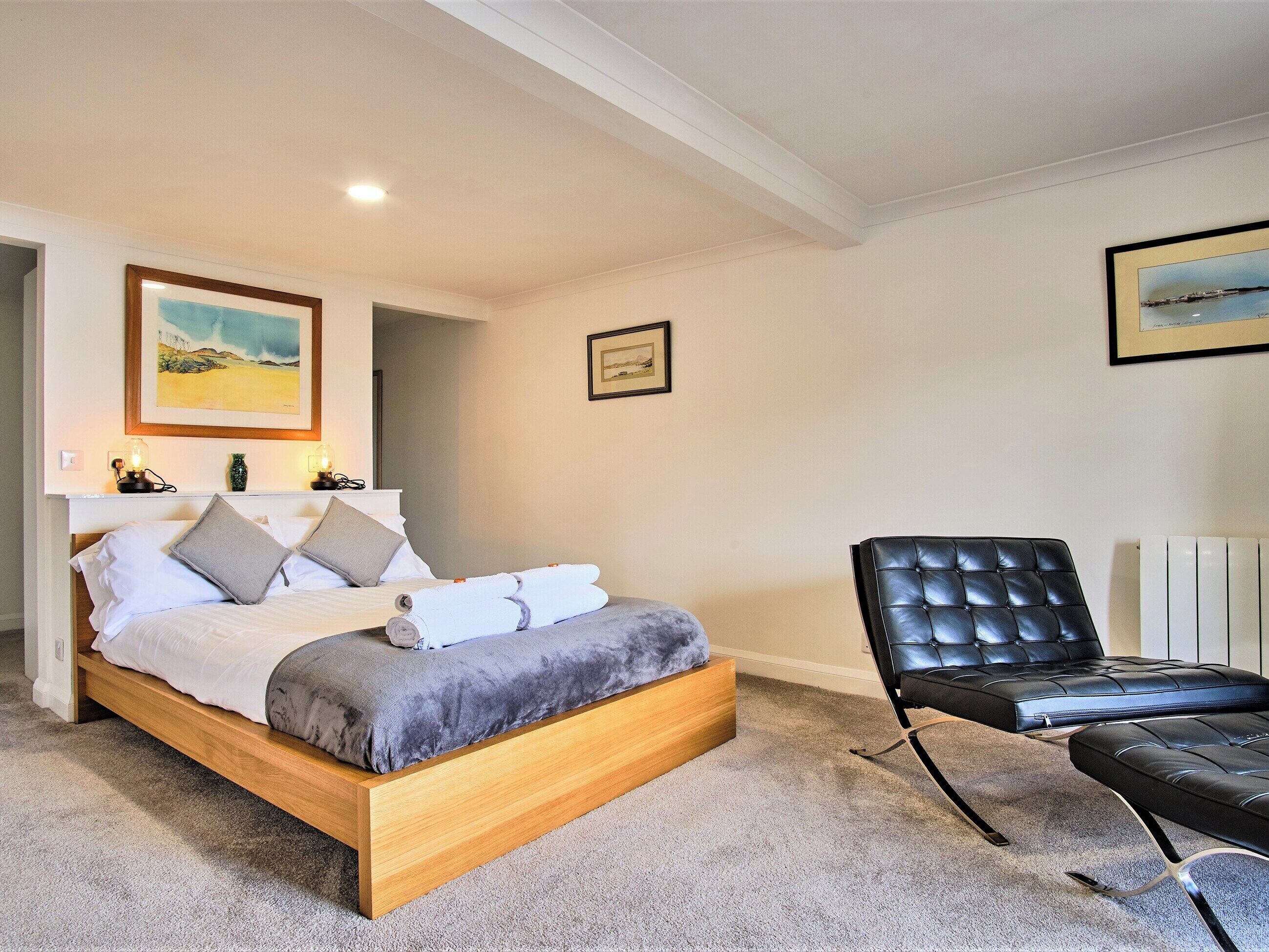 A bedroom with a wooden bed, a black leather chair, and two framed pictures on the wall.