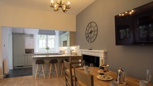 Une cuisine moderne avec un coin repas, un plancher en bois, un lustre, une horloge et un téléviseur à écran plat.