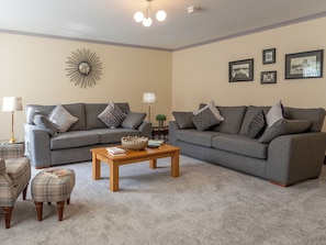Ein Wohnzimmer mit zwei grauen Sofas, einem Holztisch und einem karierten Hocker.
