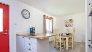 A compact kitchen with a red door, a clock, a small table with a radio, and a dining area with wooden chairs and a table.