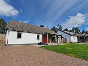 A two-story residential building with a brick driveway, a covered porch, and a small lawn area. - 3 bedroom accommodation in Aviemore (Aviemore)