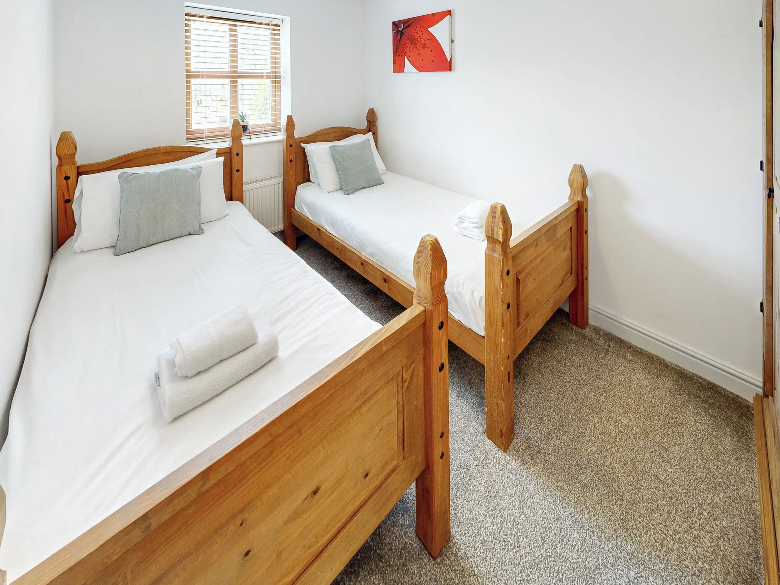 Twee houten bedden met witte lakens en grijze kussens in een kamer met een raam en een abstract rood schilderij.