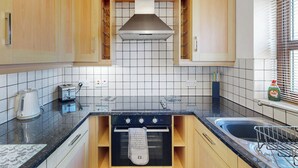 Eine kleine Küche mit Holzausstattung, einem Gasherd, einem Backofen, einer Spüle und einem Fenster mit Jalousien.