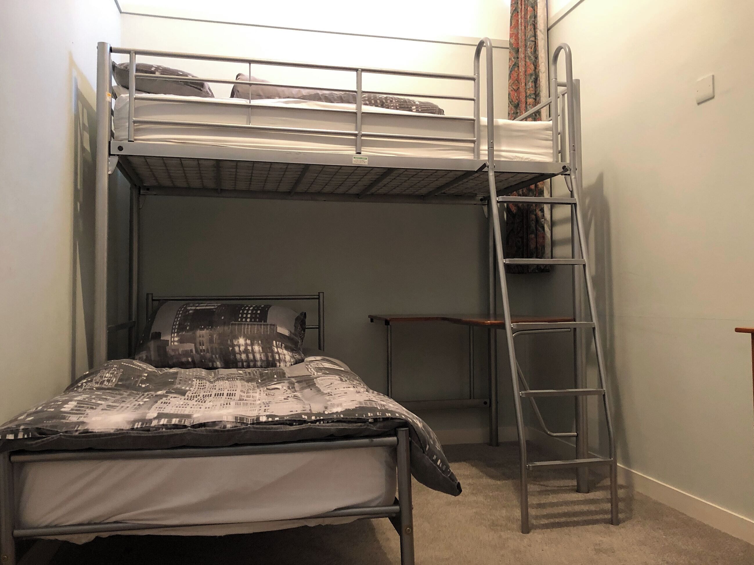 Una cama litera con escalera, un escritorio y una colcha estampada.