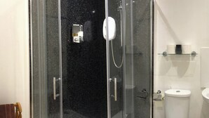 Um banheiro moderno com chuveiro em gabinete de vidro, vaso sanitário branco e uma lixeira pequena.