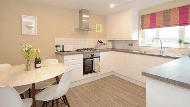 A modern kitchen with white cabinets, a dining table with chairs, a built-in oven, and a window with a decorative valance. - 1 bedroom accommodation in York (York)
