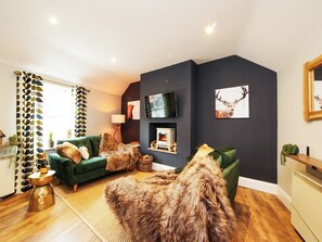 A modern living room with a dark accent wall, a green sofa, a fur rug, and a flat-screen TV mounted above a fireplace. - The Holgate Snug - UK2808 (York)