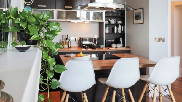 A modern kitchen with a central island, white bar stools, and a potted plant. - Seaside Apartment-UK2801 (Aberystwyth)