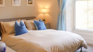 A neatly made bed with a beige comforter and blue pillows, a bedside lamp, and framed artwork on the wall. - Seaside Apartment-UK2801 (Aberystwyth)