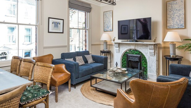 A living room with a blue sofa, wicker chairs, a glass coffee table, a fireplace, and a television. - 3 bedroom accommodation in York (York)