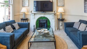 A living room with two sofas, a glass coffee table, a fireplace, and a TV mounted above it. - 3 bedroom accommodation in York (York)