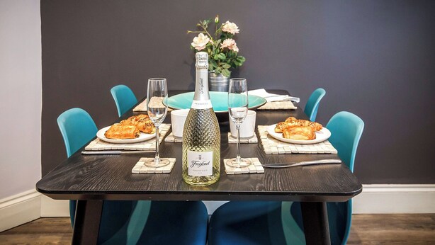 Une table à manger dressée avec des assiettes remplies de nourriture, des verres et une bouteille de vin, entourée de chaises bleues.