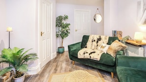 Un salon chaleureux avec un canapé vert, une plante en pot et une lampe.