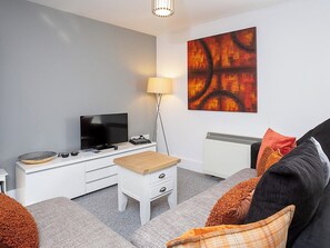 A modern living room with a flat-screen TV, a white entertainment unit, a small wooden table, a grey sofa with orange cushions, and a large abstract painting on the wall. - 2 bedroom accommodation in York (York)