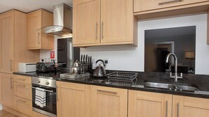 Een moderne keuken met houten kastjes, roestvrijstalen apparatuur en een zwart aanrecht.