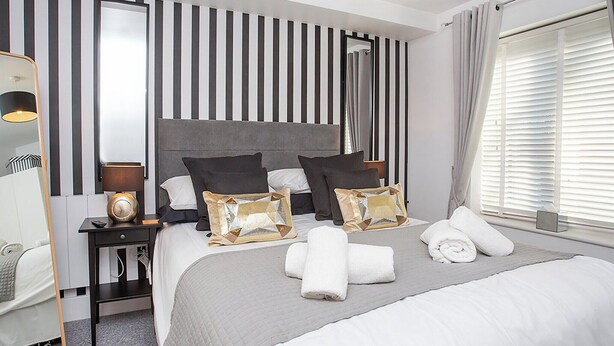 Een moderne hotelkamer met een groot bed, gestreepte wandpanelen, een nachtkastje met een lamp, en een raam met zonwering.