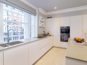 A modern kitchen with white cabinets, a built-in oven, and a large window overlooking a residential area. - The Presidential Suite (York)