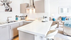 Ett modernt kök med en köksö i mitten, en matplats med en soffa och en tavla på väggen.
