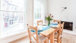 En matplats med ett träbord och stolar, en vas med blommor och utsikt över gatan genom stora fönster.