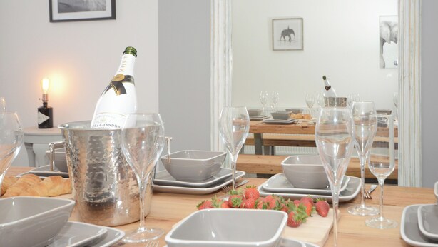 Een eettafel gedekt voor een maaltijd, met wijnglazen, een fles champagne en borden.