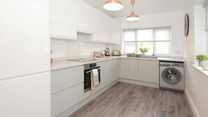 Een moderne keuken met witte kasten, een inbouwoven, een wasmachine en een raam voor natuurlijk licht.
