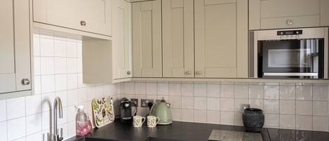 A kitchen with white cabinets, a black countertop, a built-in oven, and a kettle.