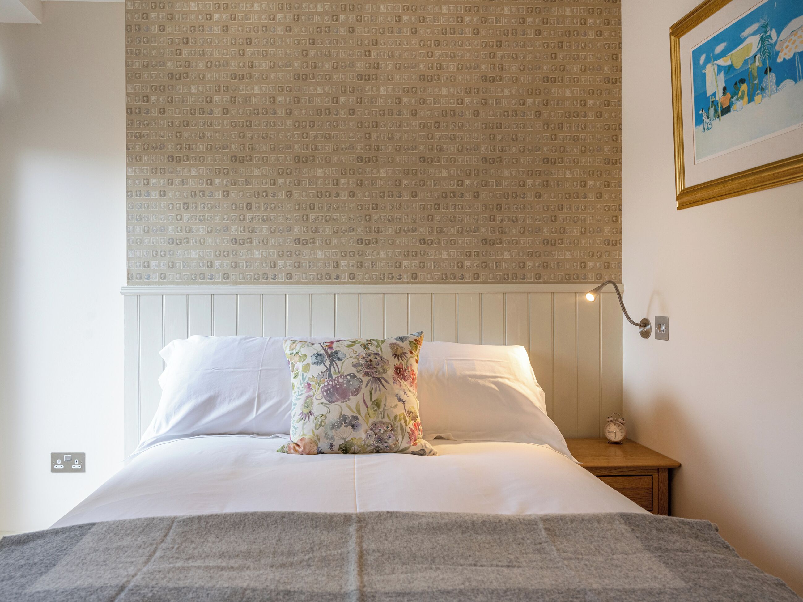 A neatly made bed with white linens, a floral pillow, and a grey blanket.