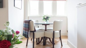 A dining area with a table and chairs, a window with blinds, and a vase with flowers. - 2 bedroom accommodation in Inverness (Inverness)
