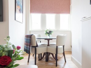 Ein Essbereich mit Tisch und Stühlen, einem Fenster mit Jalousien und einer Vase mit Blumen.